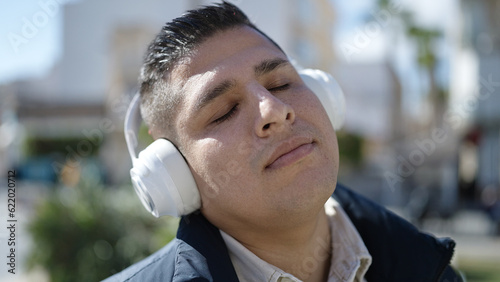 Young hispanic man listening to music at street