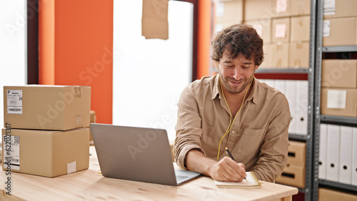 Young hispanic man ecommerce business worker having video call writing on notebook at office