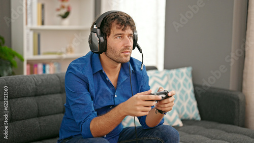 Young hispanic man playing video game sitting on sofa at home