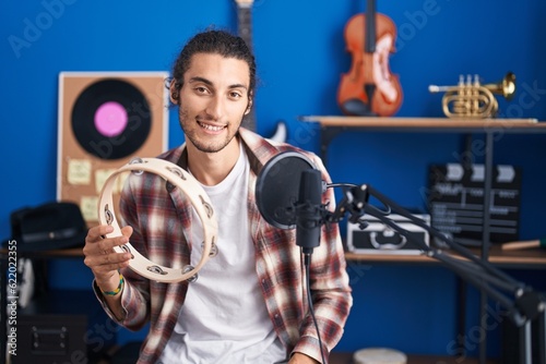 Young hispanic man musician singing song playing tambourine at music studio