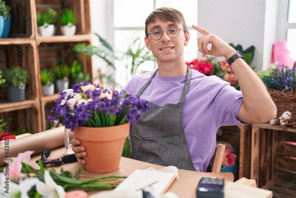 Caucasian blond man working at florist shop smiling pointing to head with one finger, great idea or thought, good memory