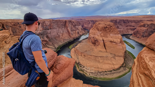 Tourist man standing at the cliff edge with panoramic aerial view of Horseshoe bend on the Colorado river near Page in summer, Arizona, USA. Incised meanders in Glen Canyon National Recreation Area photo