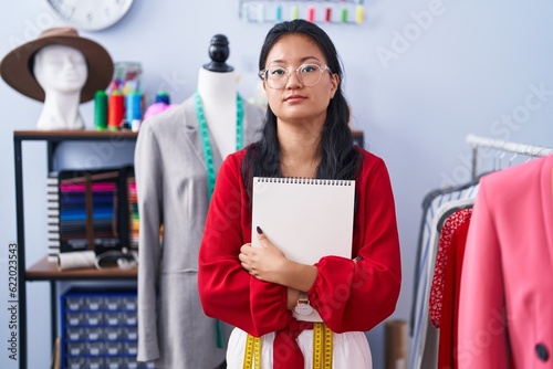 Asian young woman dressmaker standing by manikin relaxed with serious expression on face. simple and natural looking at the camera.