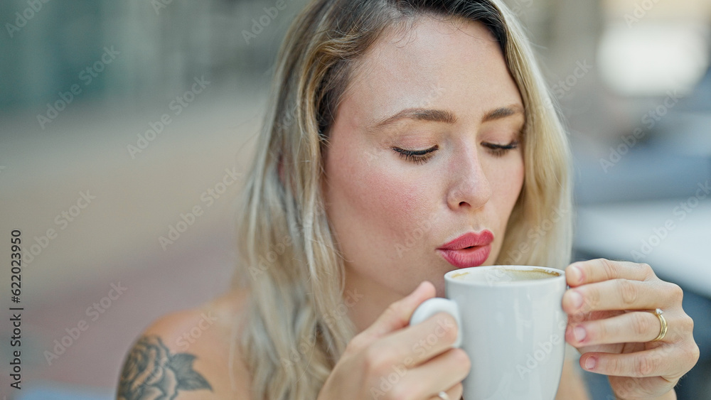 Young blonde woman blowing air to coffee at coffee shop terrace Young blonde woman blowing air to coffee at coffee shop terrace