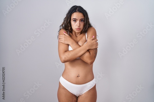 Young hispanic woman wearing white lingerie shaking and freezing for winter cold with sad and shock expression on face
