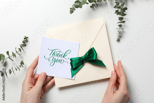 Inscription thank you on paper in hands with dried flowers on white background