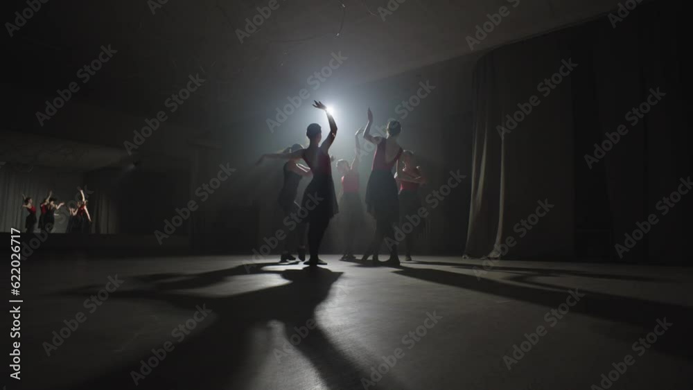 A group of ballerinas spin one after the other in a beam of light. Sharpening movements under the supervision of a trainer. High quality 4k footage