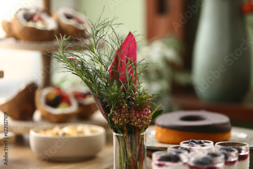 Um encantador arranjo floral com flores em tons de rosa e pequenos abacaxis decorativos, criando uma atmosfera vibrante em uma mesa de evento. photo