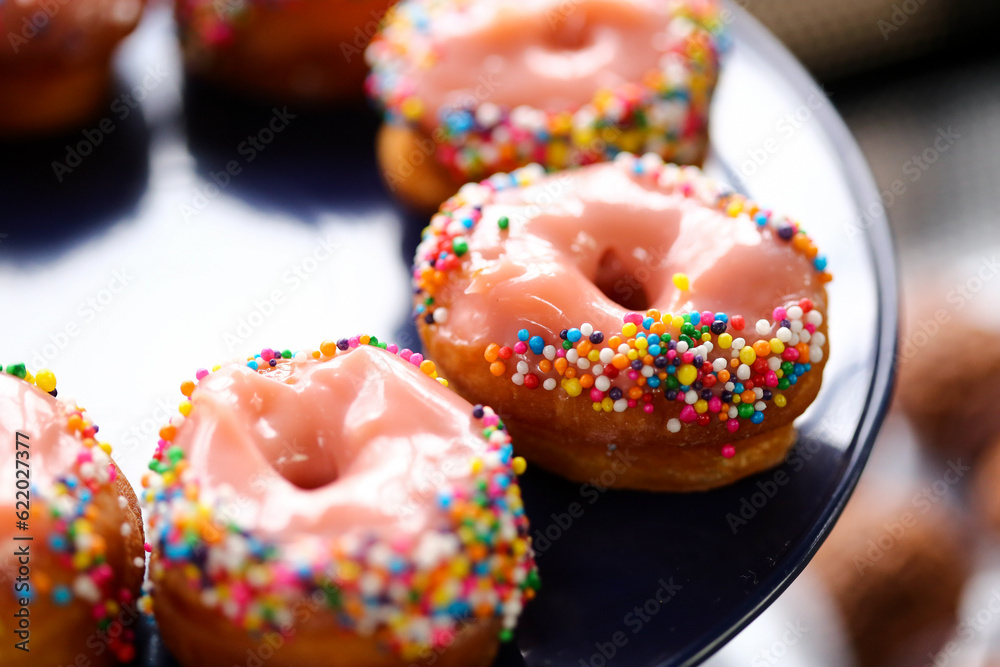 Donuts de creme cor-de-rosa cobertos com confetes coloridos, uma delícia irresistível na mesa de doces da festa infantil. Donuts de creme cor-de-rosa cobertos com confetes coloridos, uma delícia irresistível na mesa de doces da festa infantil.