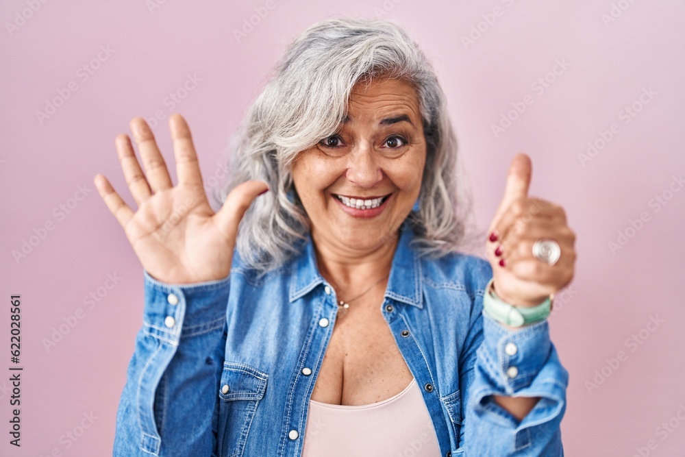 Middle age woman with grey hair standing over pink background showing and pointing up with fingers number six while smiling confident and happy. Middle age woman with grey hair standing over pink background showing and pointing up with fingers number six while smiling confident and happy.