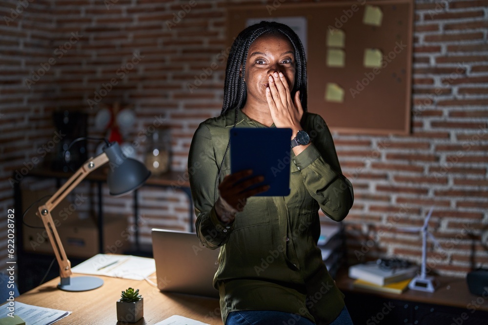 Young african american with braids working at the office at night laughing and embarrassed giggle covering mouth with hands, gossip and scandal concept Young african american with braids working at the office at night laughing and embarrassed giggle covering mouth with hands, gossip and scandal concept