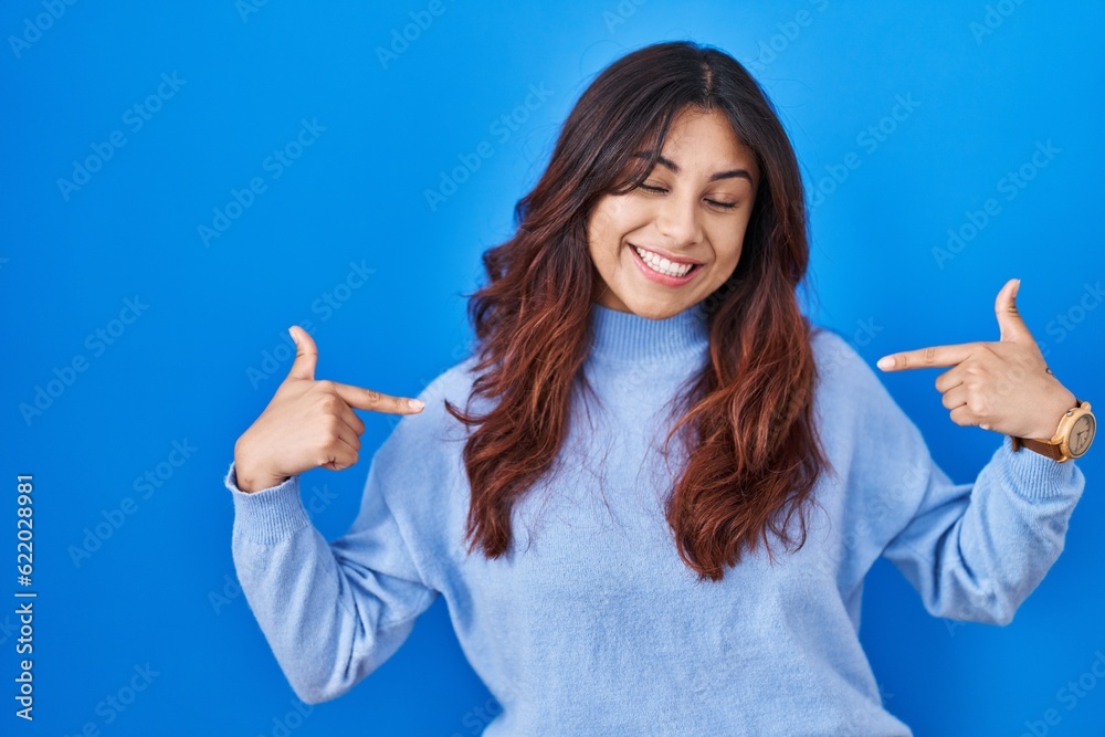 Hispanic young woman standing over blue background looking confident with smile on face, pointing oneself with fingers proud and happy. Hispanic young woman standing over blue background looking confident with smile on face, pointing oneself with fingers proud and happy.