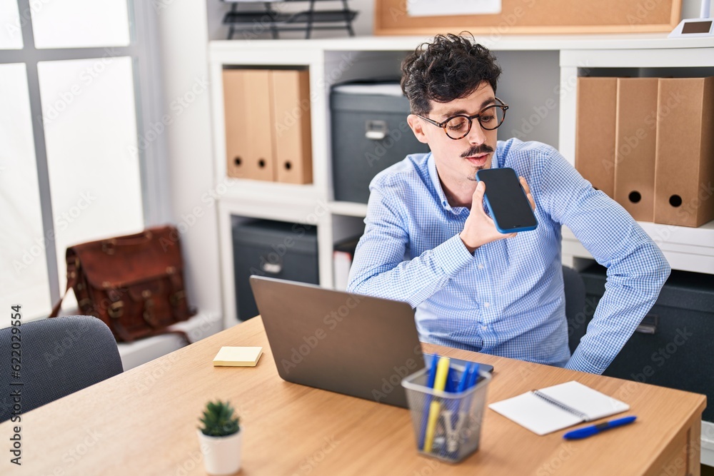 Young caucasian man business worker using laptop talking on smartphone at office Young caucasian man business worker using laptop talking on smartphone at office