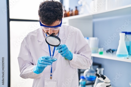 Young caucasian man scientist using magnifying glass at laboratory