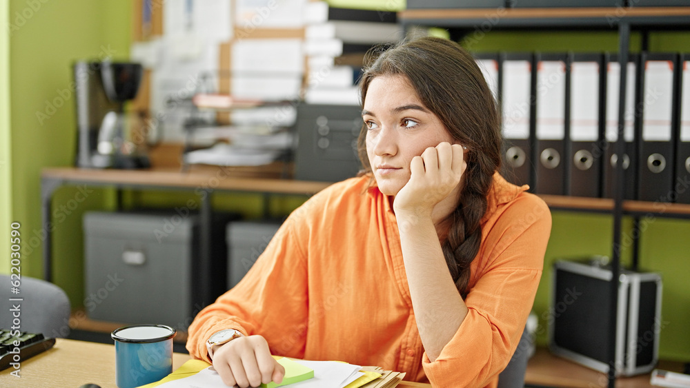 Young beautiful hispanic woman business worker sitting on table with serious face at office Young beautiful hispanic woman business worker sitting on table with serious face at office