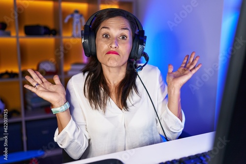 Middle age brunette woman playing video games shouting and screaming loud to side with hand on mouth. communication concept.