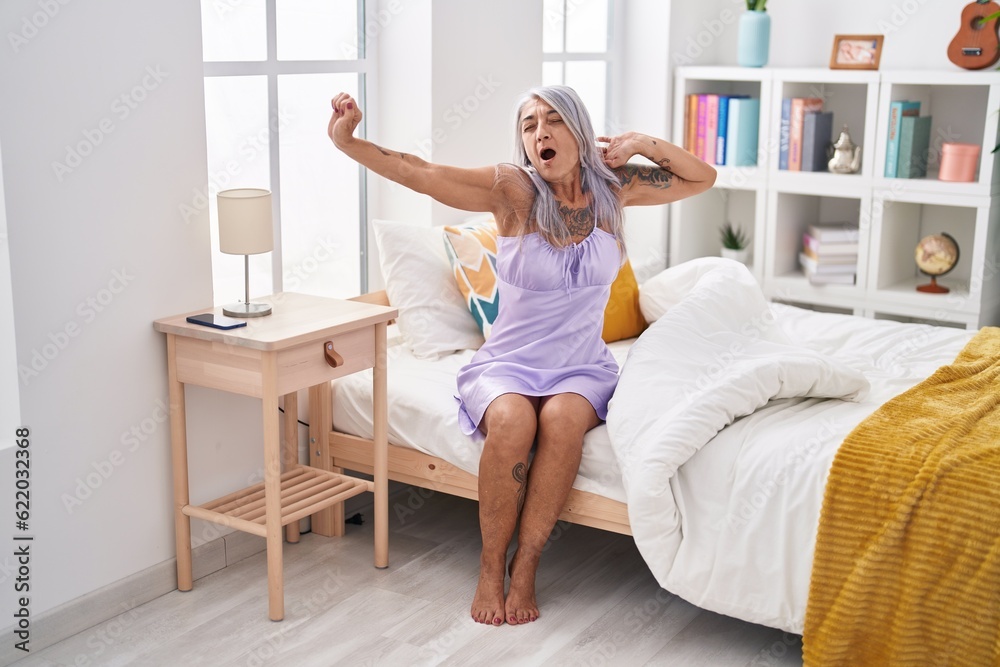 Middle age grey-haired woman waking up stretching arms yawning at bedroom Middle age grey-haired woman waking up stretching arms yawning at bedroom