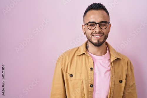 Young hispanic man standing over pink background winking looking at the camera with sexy expression, cheerful and happy face. © Krakenimages.com
