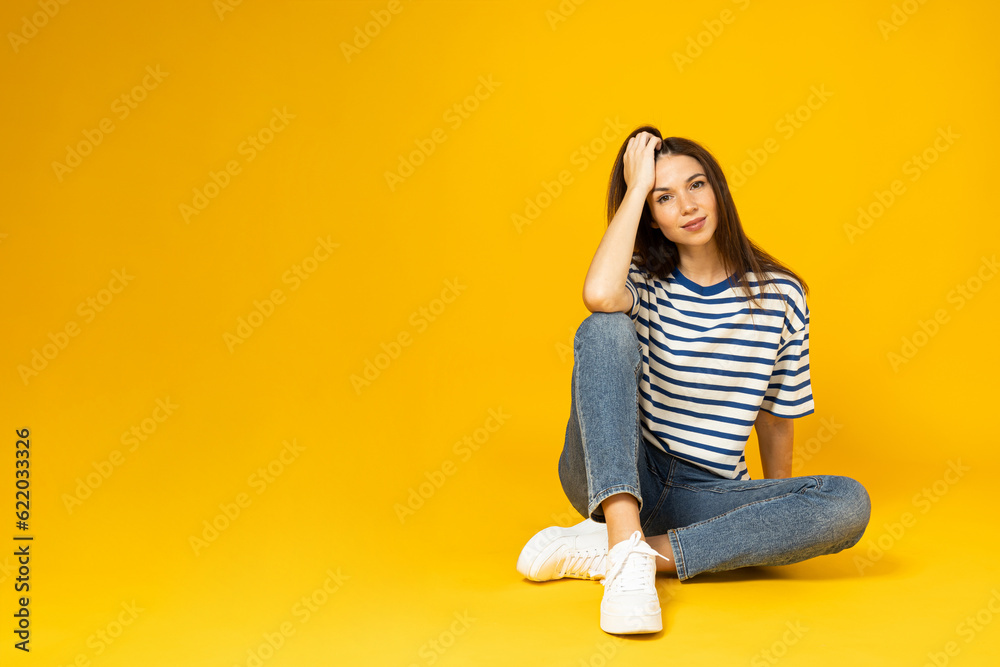 A young woman in a striped t-shirt sits on a yellow background, place for text A young woman in a striped t-shirt sits on a yellow background, place for text
