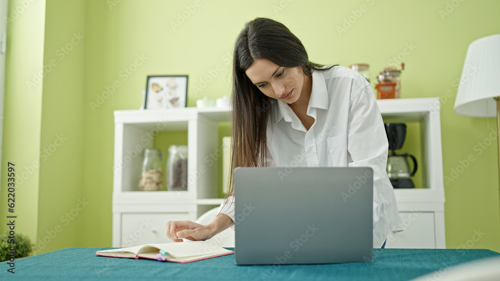 Young beautiful hispanic woman using laptop writing on notebook at dinning room Young beautiful hispanic woman using laptop writing on notebook at dinning room