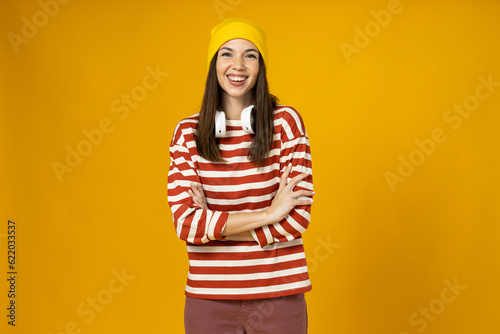 A young woman in a striped t-shirt with headphones is smiling on a yellow background