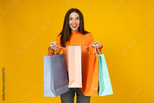 Cheerful young woman with shopping bags in her hands on a yellow background