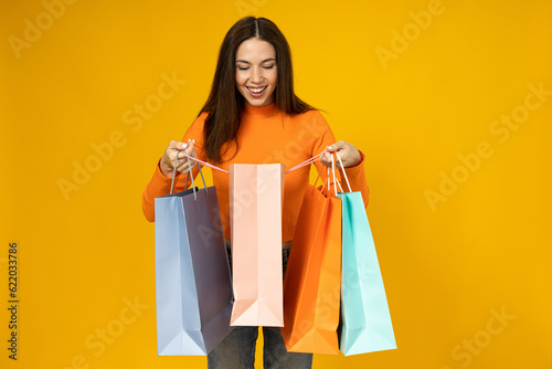 Cheerful young woman with shopping bags in her hands on a yellow background