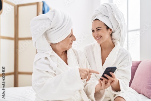 Mother and daughter wearing bathrobe using smartphone at bedroom