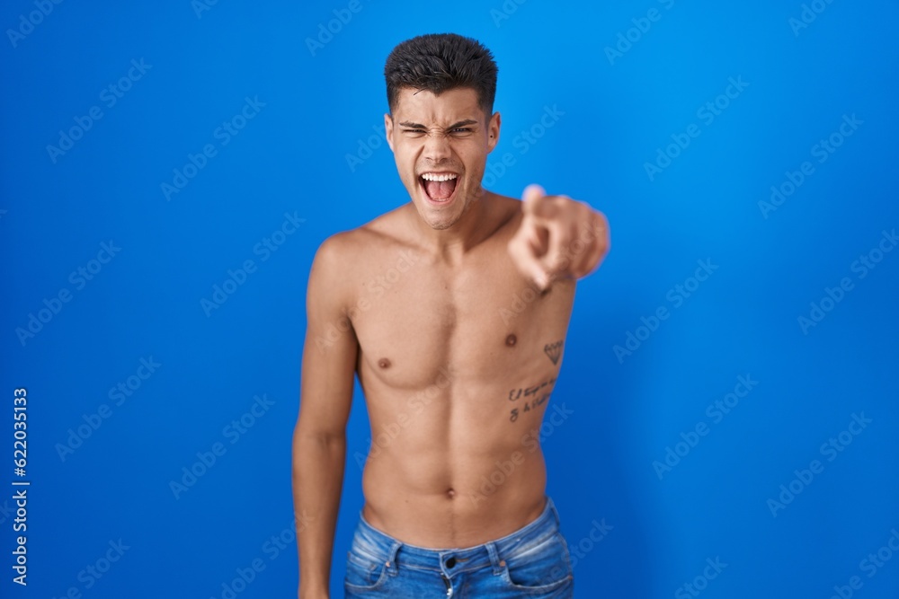 Young hispanic man standing shirtless over blue background pointing displeased and frustrated to the camera, angry and furious with you