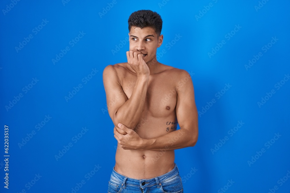 Young hispanic man standing shirtless over blue background looking stressed and nervous with hands on mouth biting nails. anxiety problem. Young hispanic man standing shirtless over blue background looking stressed and nervous with hands on mouth biting nails. anxiety problem.