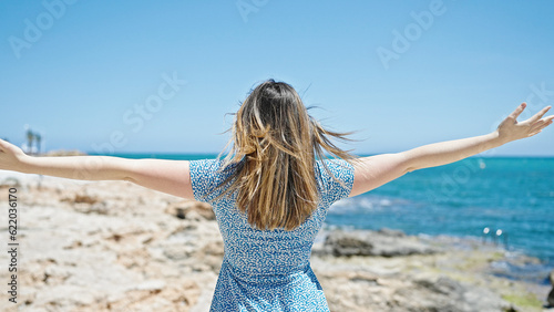 Young blonde woman tourist standing backwards wirh arms open at seaside