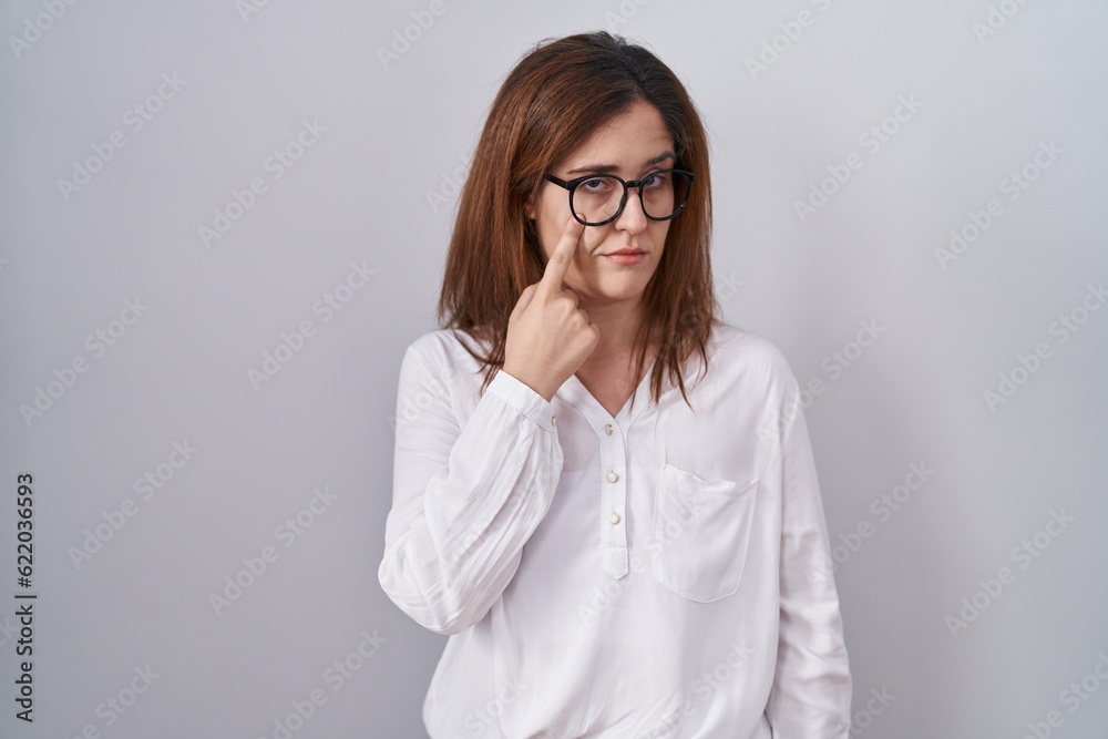 Brunette woman standing over white isolated background pointing to the eye watching you gesture, suspicious expression Brunette woman standing over white isolated background pointing to the eye watching you gesture, suspicious expression