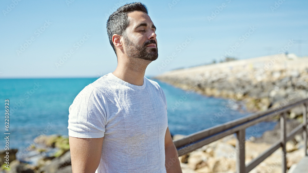 Young hispanic man breathing with closed eyes at seaside
