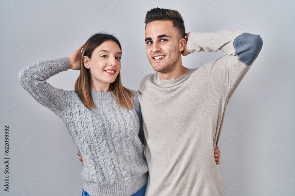 Young hispanic couple standing over white background smiling confident touching hair with hand up gesture, posing attractive and fashionable