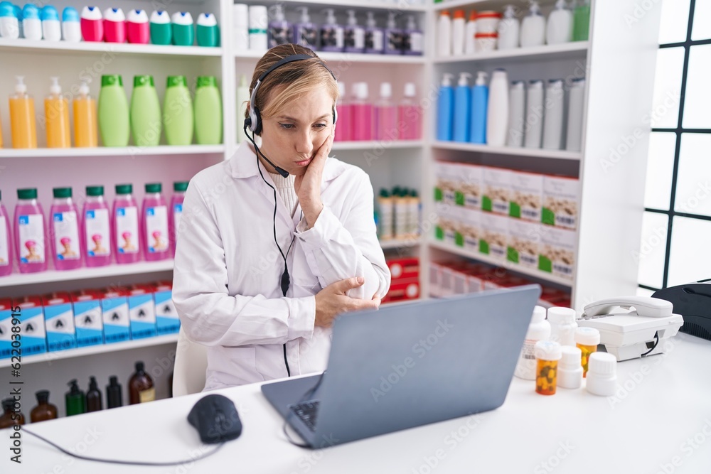 Young caucasian woman working at pharmacy drugstore using laptop thinking looking tired and bored with depression problems with crossed arms.