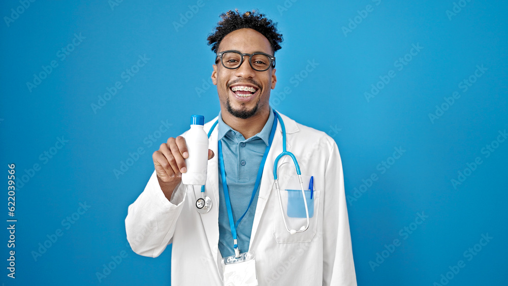 African american man doctor smiling confident holding medication bottle over isolated blue background African american man doctor smiling confident holding medication bottle over isolated blue background