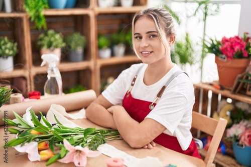 Young blonde woman florist smiling confident sitting with arms crossed gesture at flower shop