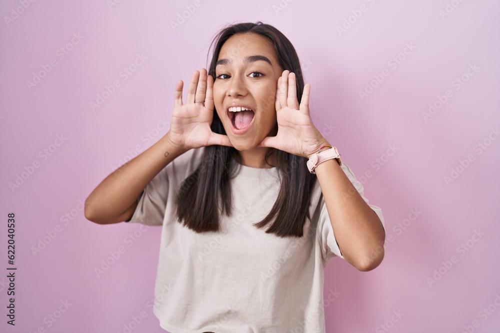 Young hispanic woman standing over pink background smiling cheerful playing peek a boo with hands showing face. surprised and exited