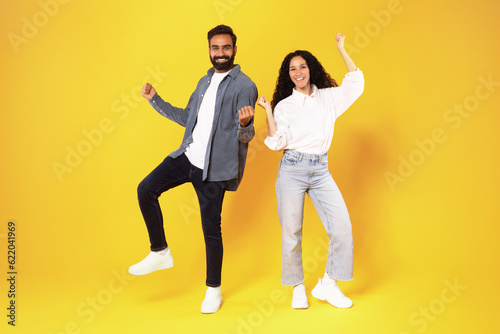 Arab Spouses Shaking Fists In Joy Posing Over Yellow Background