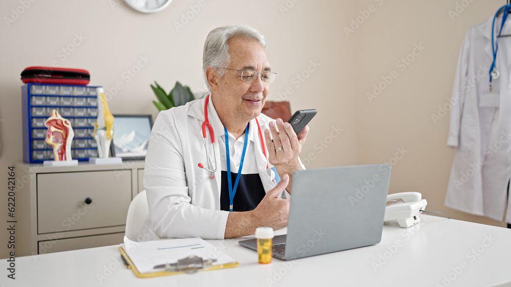 Middle age man with grey hair doctor sending voice message with smartphone at clinic