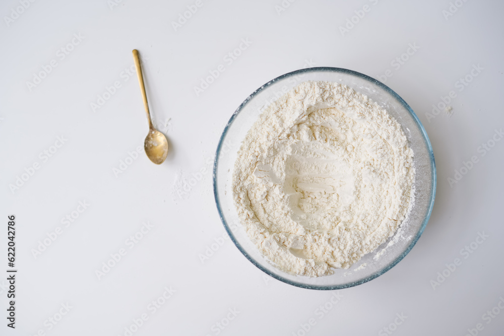 Preparing the dough, white flour in a bowl on a white background with a spoon of ingredients, ready to cook. Start of cooking with flour Preparing the dough, white flour in a bowl on a white background with a spoon of ingredients, ready to cook. Start of cooking with flour
