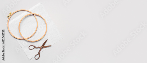 Wooden embroidery hoops with canvas and scissors on light background with space for text