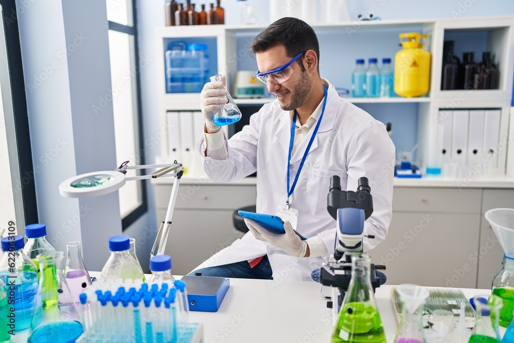 Young hispanic man scientist measuring liquid using touchpad at laboratory Young hispanic man scientist measuring liquid using touchpad at laboratory