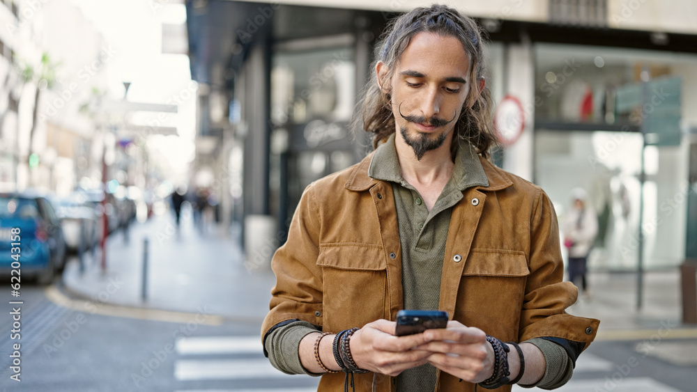 Fototapeta premium Young hispanic man using smartphone with serious expression at street