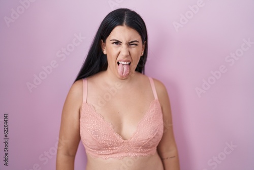 Young hispanic woman wearing pink bra sticking tongue out happy with funny expression. emotion concept.
