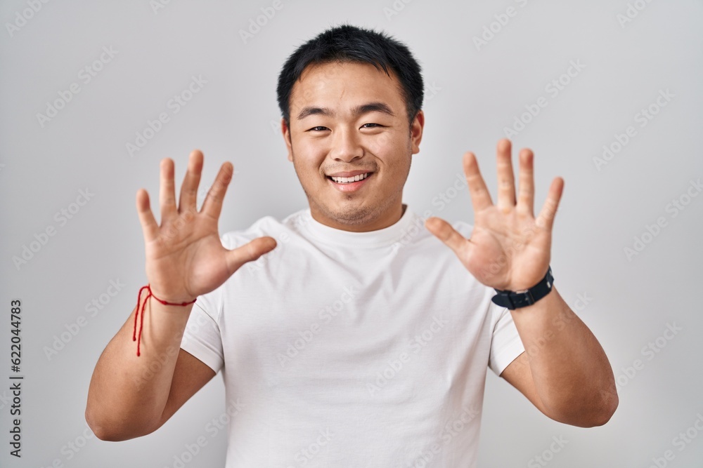 Young chinese man standing over white background showing and pointing up with fingers number ten while smiling confident and happy. Young chinese man standing over white background showing and pointing up with fingers number ten while smiling confident and happy.