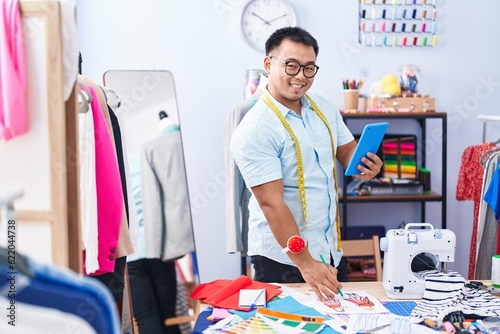 Young chinese man tailor using touchpad drawing clothing design at tailor shop