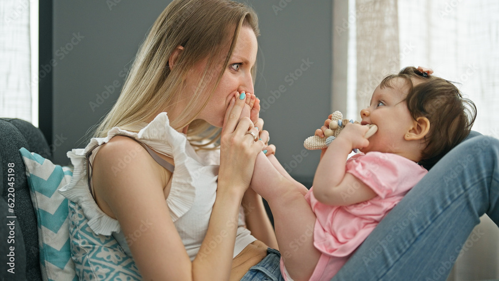 Mother and daughter sitting on sofa playing together kissing feet at home