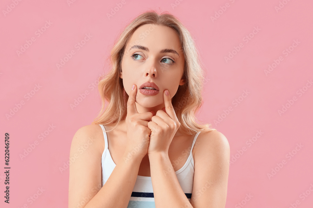 Young woman doing face building exercise on pink background, closeup