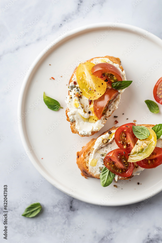 Bruschetta sandwiches with tomatoes, cream cheese, olive oil and basil on a plate on white marble background, top view, copy space. Traditional italian antipasti